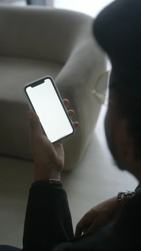 a man sitting on a couch holding a cell phone, pexels, gradient white to silver, dark-skinned, square, iphone 12