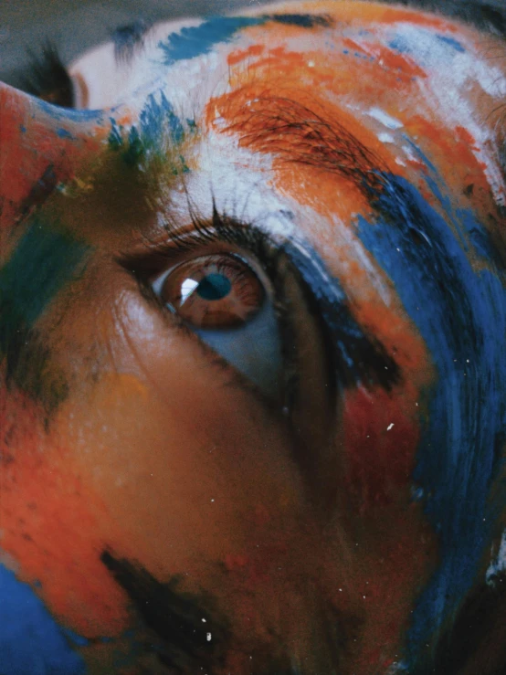 a close up of a person with paint on their face, a photorealistic painting, trending on pexels, orange and blue, album cover, eye reflection, high angle shot