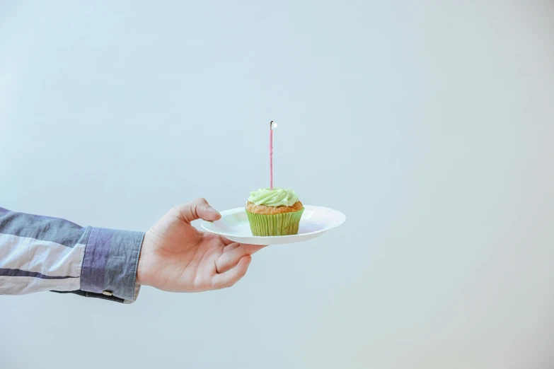 a person holding a plate with a cupcake on it, by Nicolette Macnamara, unsplash, postminimalism, happy birthday, green, shot on sony a 7, 🍸🍋