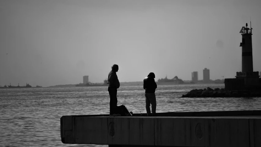 a couple of people standing on top of a pier, a black and white photo, people angling at the edge, new york harbour, praying, sad men