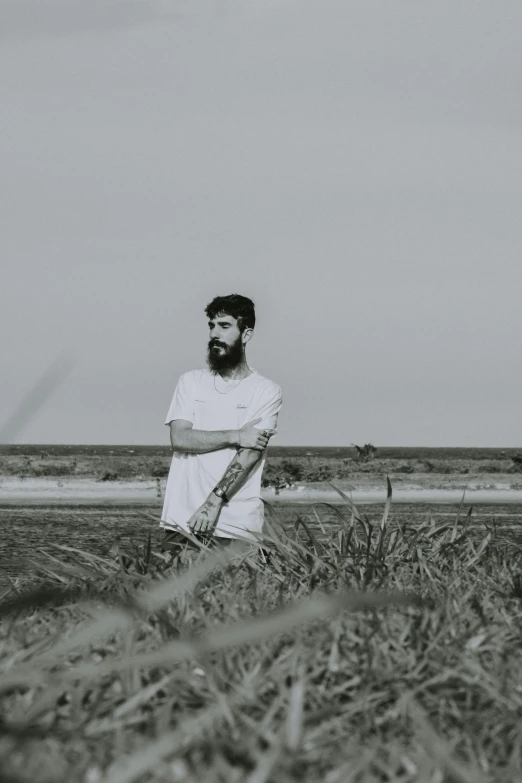 a man standing in a field of tall grass, a black and white photo, unsplash, minimalism, zayn malik, at a beach, bearded, ilustration