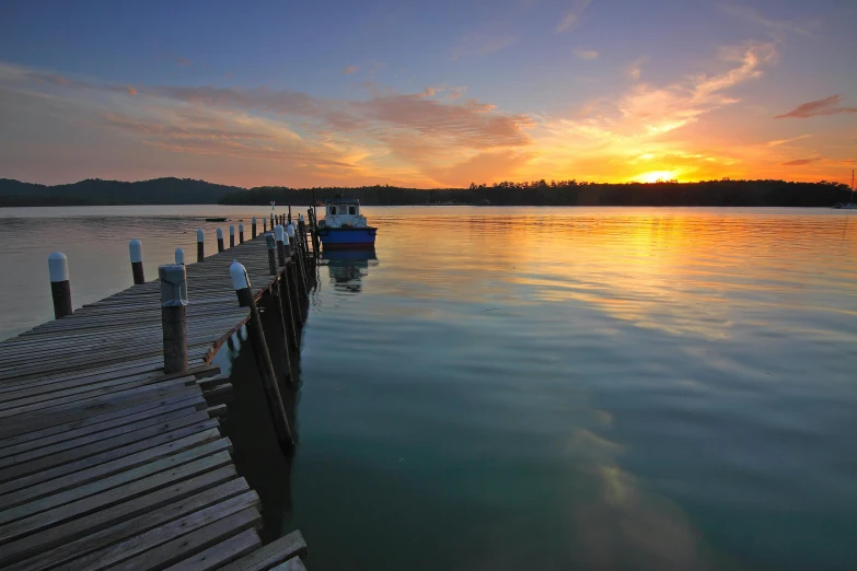 a boat sitting on top of a body of water, inspired by Edwin Georgi, pexels contest winner, hurufiyya, near a jetty, soft glow, picton blue, sunset lighting