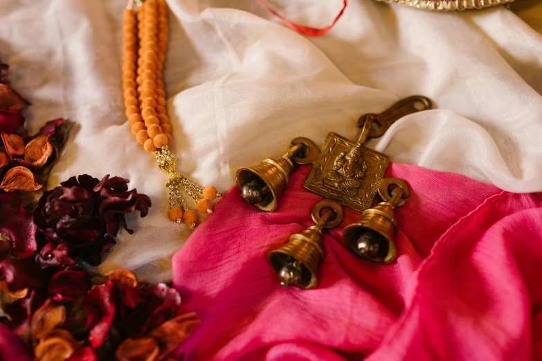 a bunch of jewelry sitting on top of a bed, a still life, by Alice Mason, unsplash, hurufiyya, in a temple, pink and orange, wedding, bells