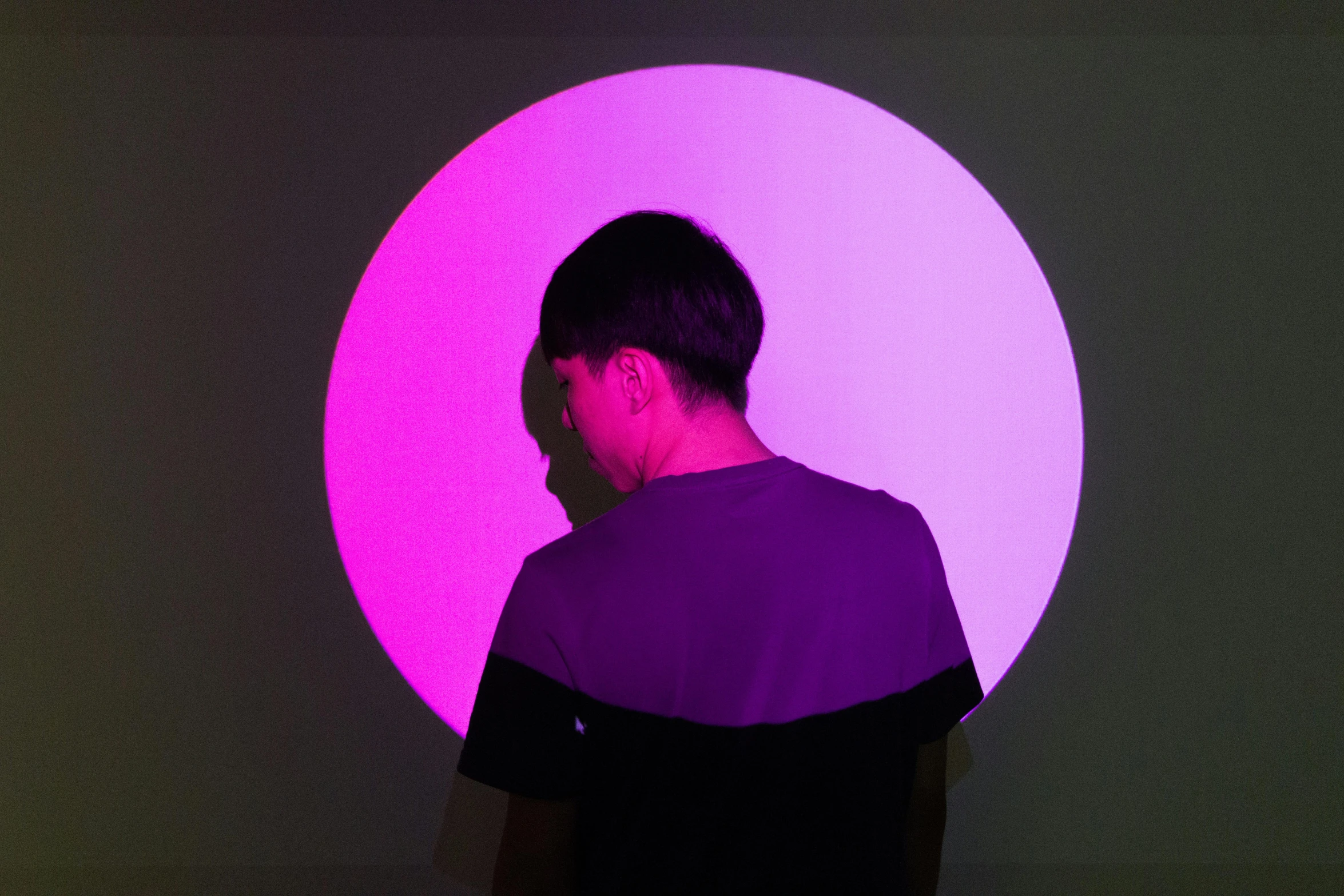 a man standing in front of a purple light, inspired by Russell Dongjun Lu, pexels contest winner, interactive art, circle, set on singaporean aesthetic, looking across the shoulder, half turned around