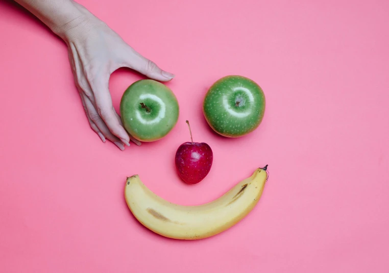 a smiley face made out of apples and a banana, trending on pexels, green and pink colour palette, 💋 💄 👠 👗, sleek hands, magical mood