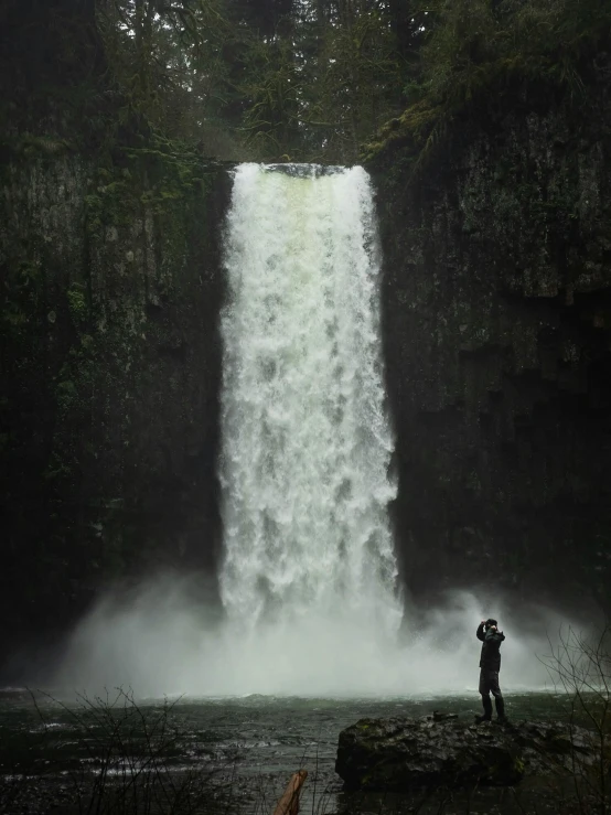 a man standing on a rock in front of a waterfall, an album cover, unsplash contest winner, oregon, taken in the late 2010s, alana fletcher, towering over the camera