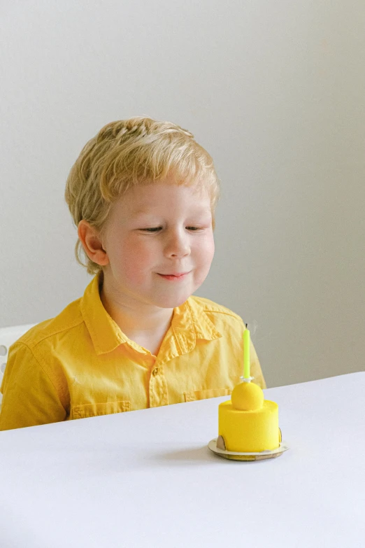 a little boy that is sitting at a table, holding a yellow toothbrush, holding a candle holder, solid coloured shapes, cake