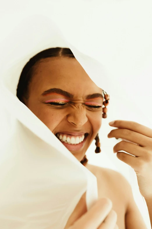 a woman covering her face with a sheet, an album cover, by Olivia Peguero, trending on pexels, happening, brown skin man with a giant grin, dewy skin, laughing and joking, putting makeup on