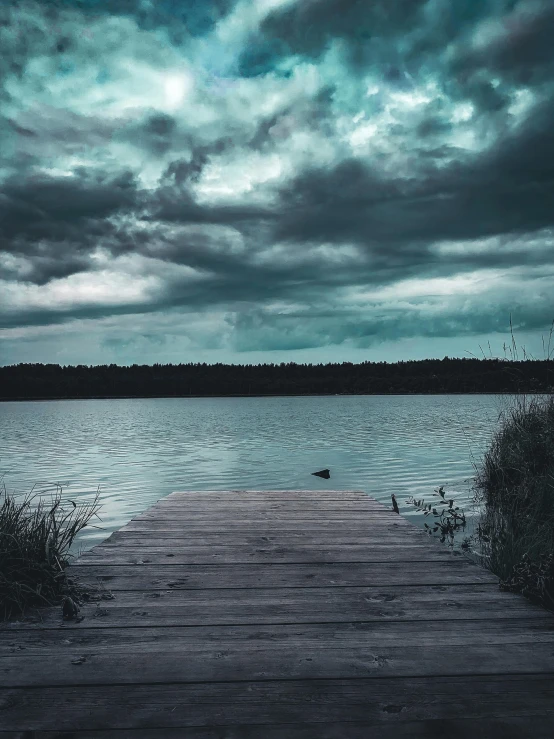a dock in the middle of a lake under a cloudy sky, a picture, inspired by Elsa Bleda, pexels contest winner, romanticism, menacing look, dark image, teal aesthetic, old photo of a creepy landscape