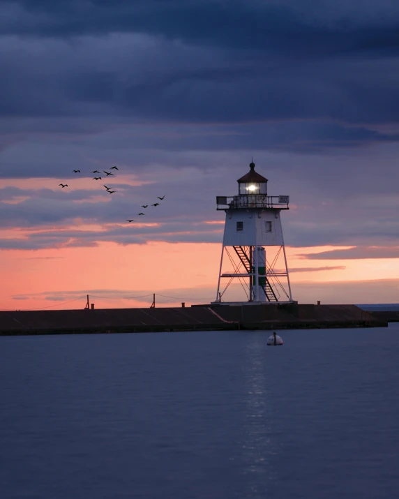 a light house sitting on top of a body of water, a colorized photo, by Jacob Burck, pexels contest winner, dusk sky, flying birds in the distance, midwest town, lgbtq