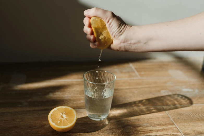 a person squeezing a lemon into a glass of water, pexels, back of hand on the table, ash thorp, natural tpose, thumbnail