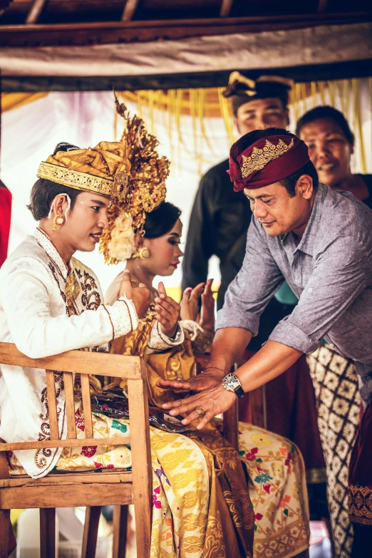 a man sitting on top of a wooden chair next to a woman, pexels contest winner, sumatraism, intricate gold headdress, ceremony, square, banner