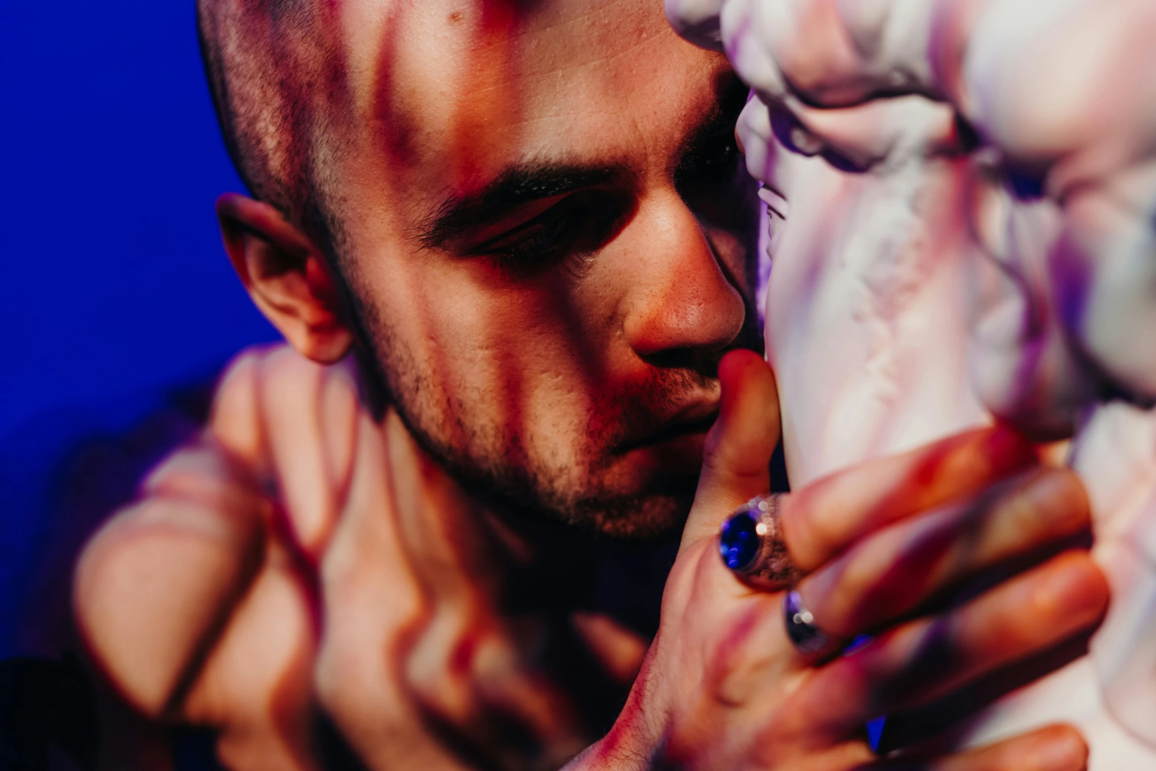 a close up of a person holding a statue, a tattoo, by Adam Marczyński, bisexual lighting, male face and bust, shaved temple, colored photography