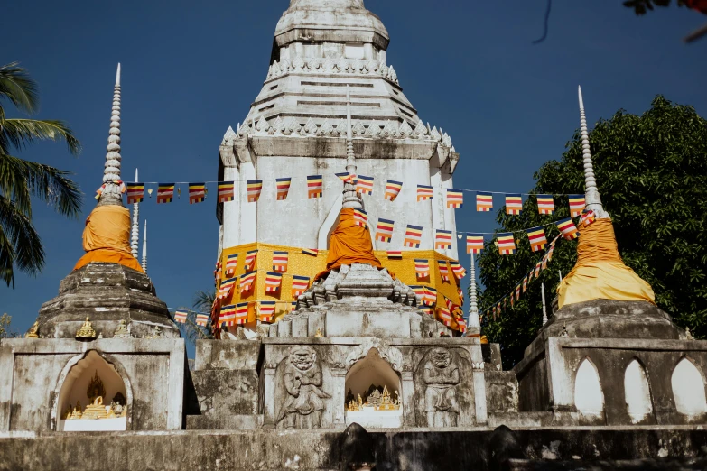 a couple of people that are standing in front of a building, unsplash contest winner, samikshavad, thai temple, white and orange, square, prayer flags