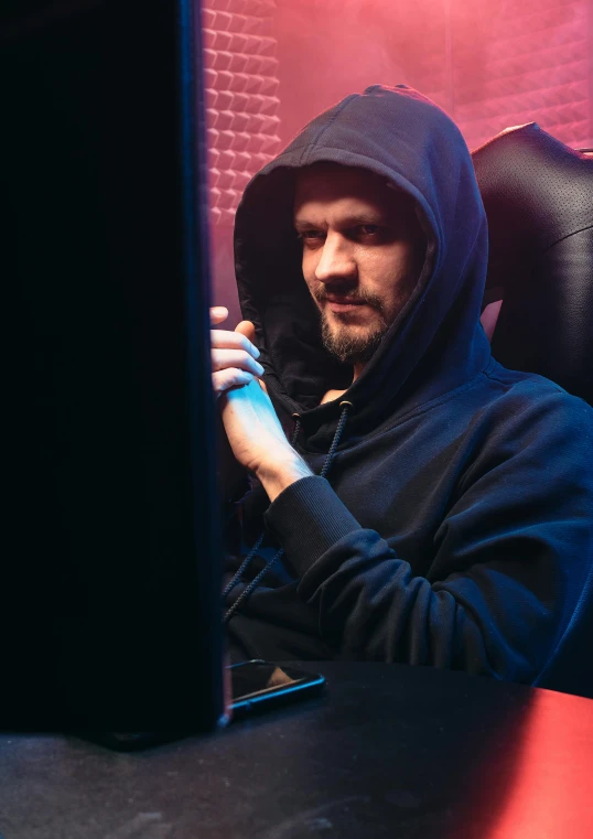 a man sitting in front of a laptop computer, featured on reddit, realism, e-sport style, in a black hoodie, wearing nanotech honeycomb robe, thumbnail