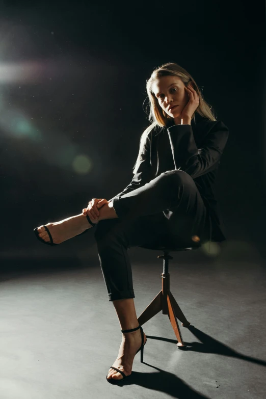 a woman sitting on top of a wooden chair, a portrait, trending on unsplash, wearing in black clothes, lights on, in style of britt marling, tailored clothing