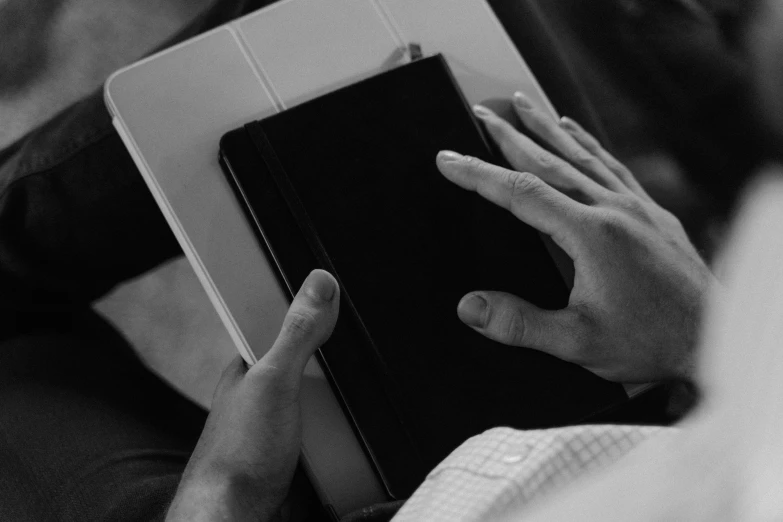 a black and white photo of a person holding a book, a black and white photo, took on ipad, hands of men, teaser, holding books