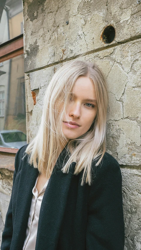 a woman standing in front of a stone wall, inspired by Louisa Matthíasdóttir, unsplash contest winner, photorealism, sleek blond hair, medium long bob, photo of a model, vitaly bugarov