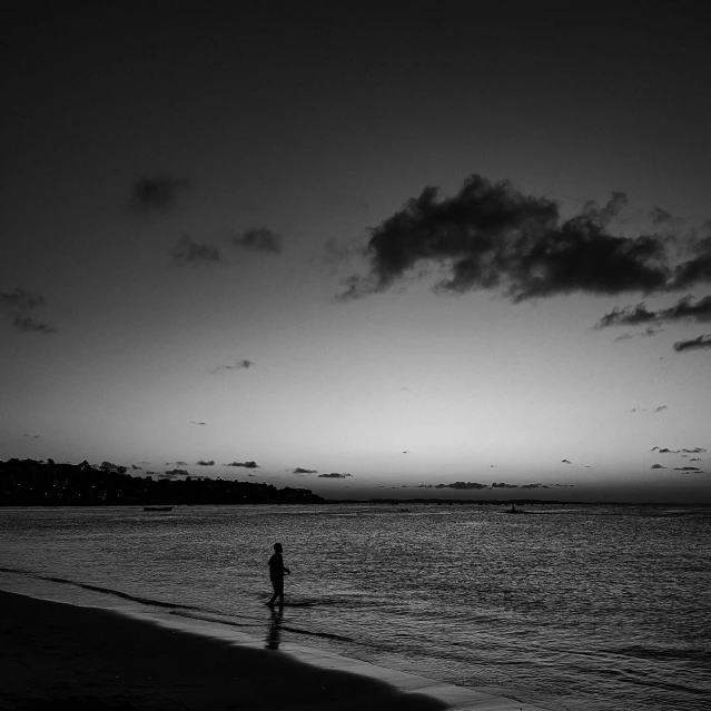 a person standing on top of a beach next to the ocean, a black and white photo, during dawn, jamaica, during the night, people in beach