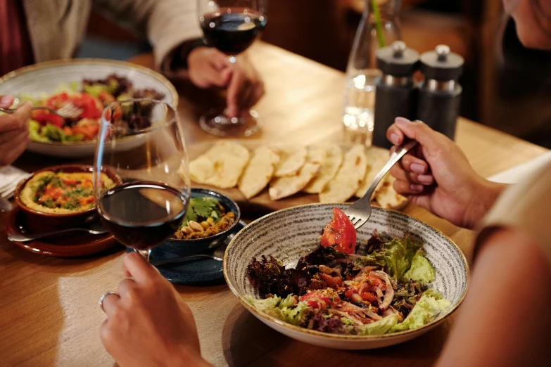 a group of people sitting at a table with plates of food, by Carey Morris, pexels contest winner, holding a glass of red wine, black and terracotta, bowl filled with food, lachlan bailey