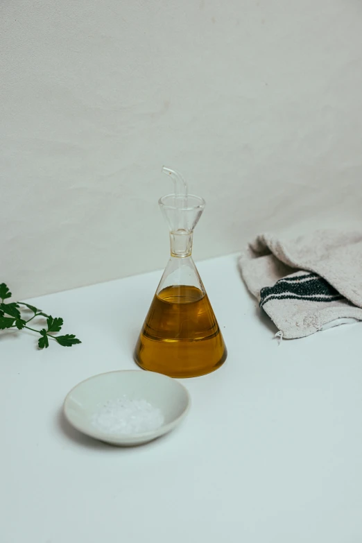 a bottle of oil sitting on top of a white table, inspired by Ceferí Olivé, unsplash, glass tableware, made of lab tissue, organic dress, minimal kitchen