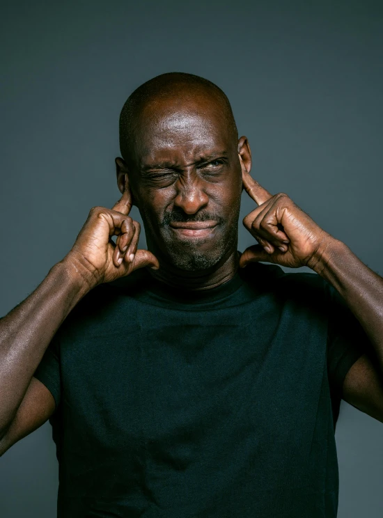 a man holding his hands to his ears, trending on pexels, les nabis, lance reddick, irritated expression, he is wearing a black t-shirt, balding