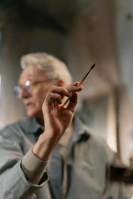 a man holding a pair of scissors in his hand, a photorealistic painting, by David Simpson, pexels contest winner, an oldman, holding a paintbrush, looking to the right, handcrafted