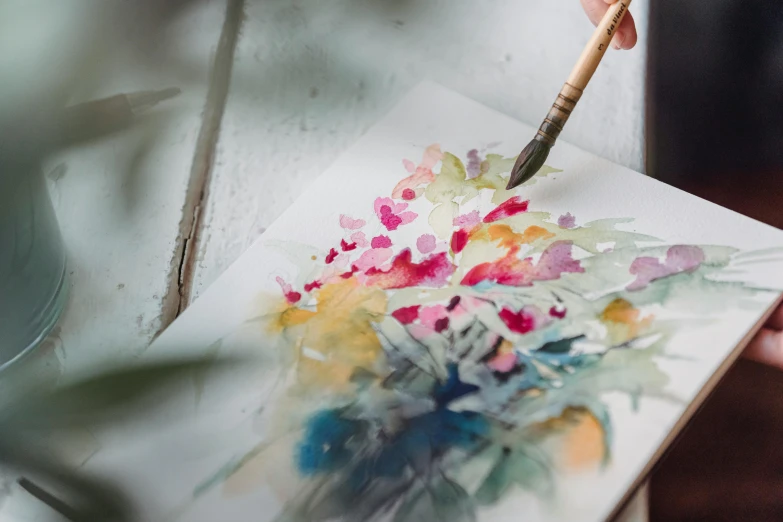 a person painting with a brush on a piece of paper, a watercolor painting, trending on pexels, visual art, bouquet, blurry and dreamy illustration, thick painting, floral splash painting