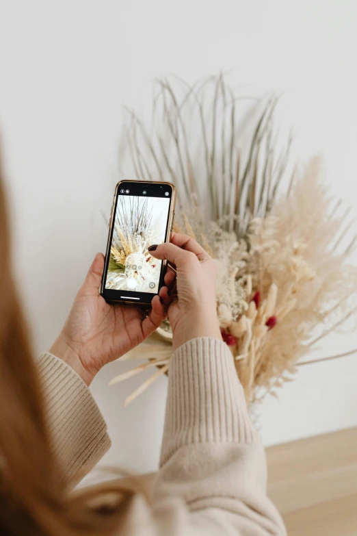 a woman taking a picture with her cell phone, trending on pexels, visual art, dried plants, textured base ; product photos, inspect in inventory image, with flowers and plants