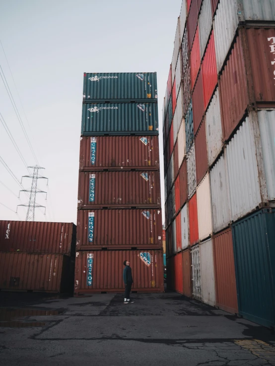 a person standing in front of a stack of shipping containers, pexels contest winner, trending on r/streetwear, low quality photo, tall towers, video footage