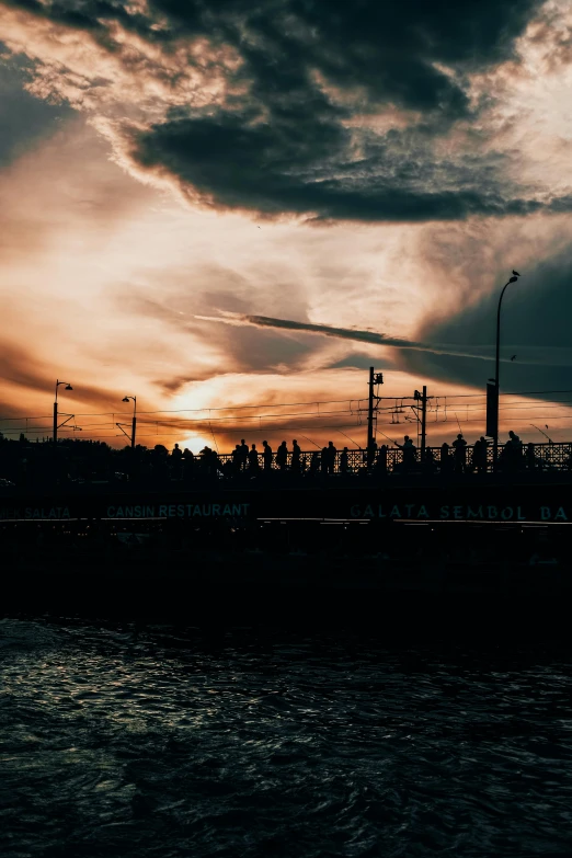 a large body of water under a cloudy sky, a picture, pexels contest winner, happening, crowded silhouettes, bridge, sunset!, silhouette :7