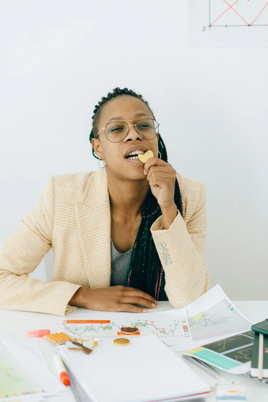 a woman sitting at a table eating a donut, wearing a suit and glasses, african canadian, eating mars bar candy, architect