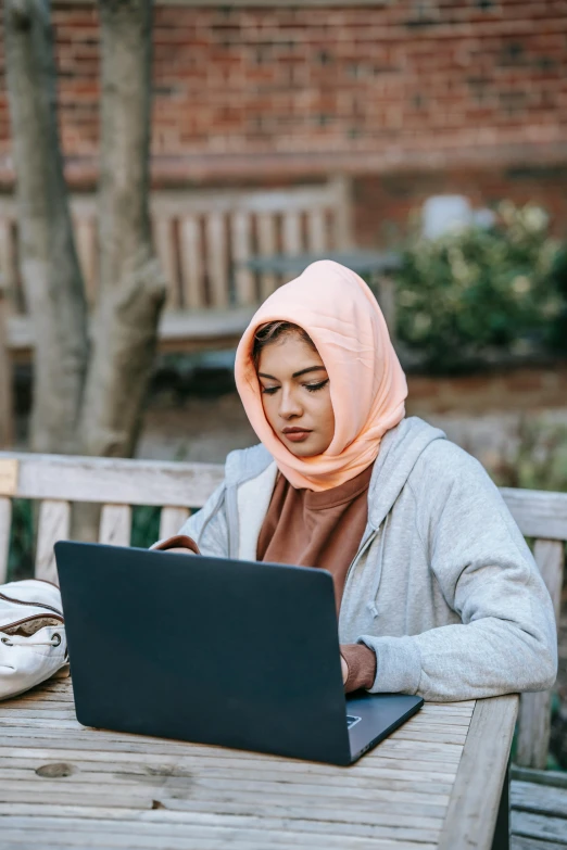 a woman sitting at a table with a laptop, hurufiyya, sitting on a park bench, wearing a head scarf, computer science, 2019 trending photo