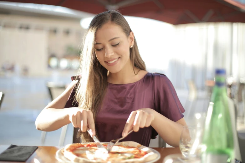 a woman sitting at a table with a plate of pizza, profile image, people outside eating meals, grey, subtle smile