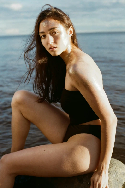 a woman is sitting on a rock by the water, unsplash, renaissance, black swimsuit, portrait sophie mudd, loosely cropped, ad image