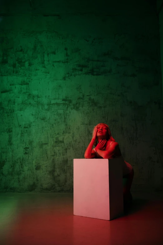 a man sitting on top of a white box, an album cover, inspired by Elsa Bleda, unsplash, video art, green bright red, body and head in view, ( ( theatrical ) ), on the stage