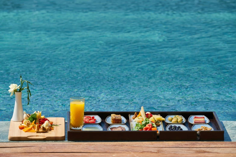 a tray of food sitting on top of a wooden table next to a pool, unsplash, azure blue water, breakfast buffet, vibrant blue, sunken