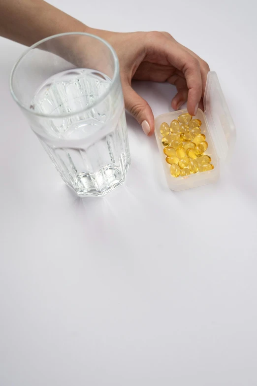 a person holding a container of fish oil next to a glass of water, by Andries Stock, yellow gemstones, opening shot, contain, qualia