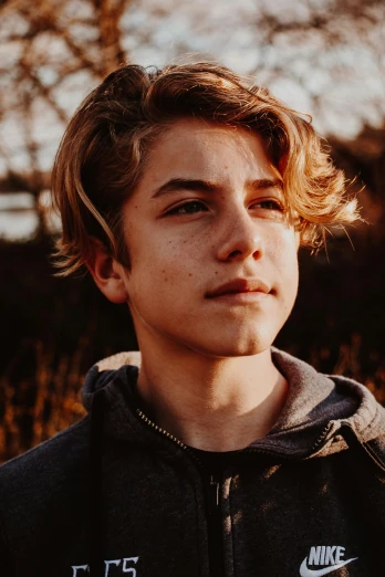 a close up of a person wearing a hoodie, by Jacob Toorenvliet, trending on pexels, portrait of 14 years old boy, at golden hour, boy hair, beth harmon