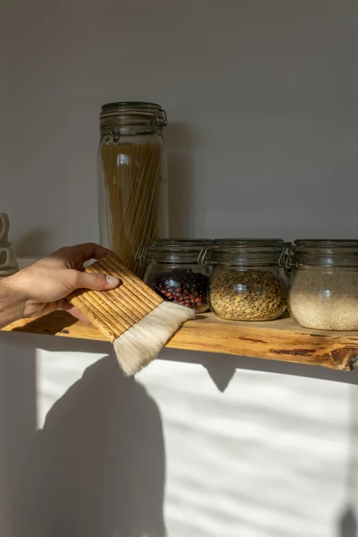 a person brushing a brush on top of a counter, by Jessie Algie, hyperrealism, simple wood shelves, scarf made from spaghetti, sustainability, snacks