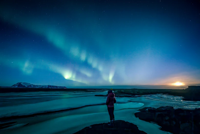 a person standing on top of a rock under the aurora lights, blue and green colours, waves of lights, facing away, nordic