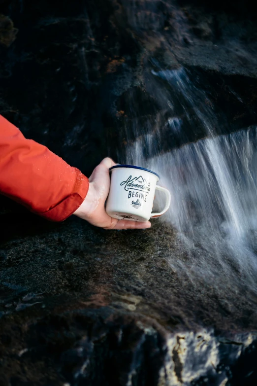 a person holding a cup near a stream of water, by Jessie Algie, official product photo, adventure, white mug, detailed information