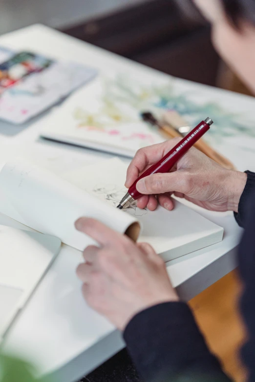 a person sitting at a table writing on a piece of paper, arbeitsrat für kunst, silver and crimson ink, designer product, shodo, fine point pen