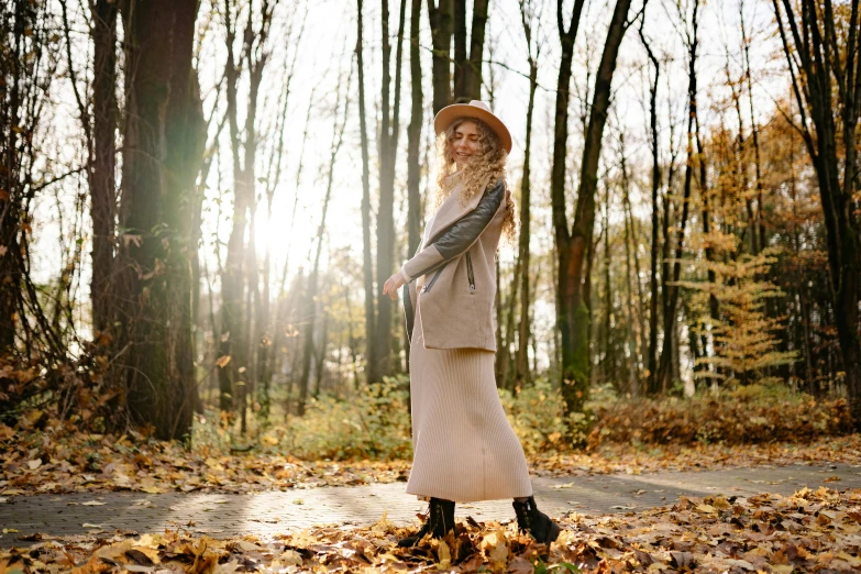 a woman standing in the middle of a forest, trending on pexels, straw hat and overcoat, dressed in long fluent skirt, autumn season, sunny day in a park