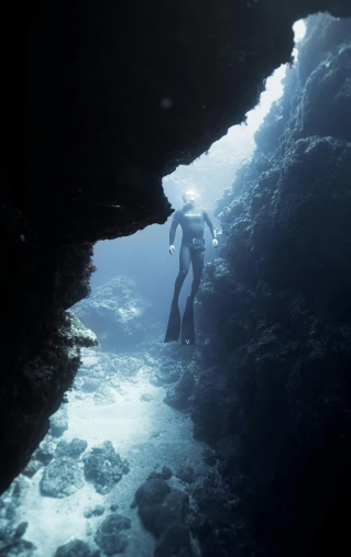 a person that is standing in the water, cavern ceiling visible, coral sea bottom, walking to the right, ben ridgway