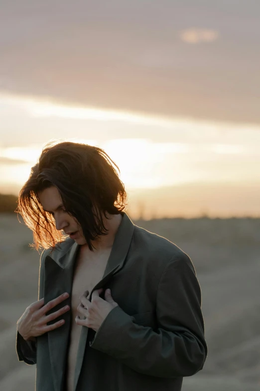 a woman standing on top of a sandy beach, an album cover, inspired by Elsa Bleda, unsplash, beautiful androgynous girl, jacket over bare torso, sunset in the desert, julian ope