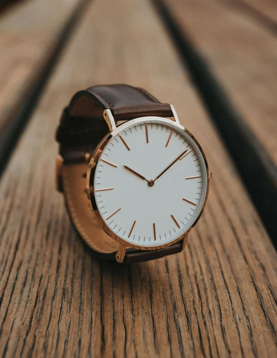 a watch sitting on top of a wooden table, by Robbie Trevino, unsplash contest winner, brown and white color scheme, product view, gold, close up front view