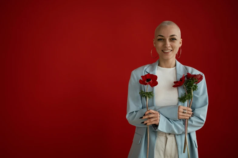 a woman standing in front of a red wall holding a bunch of roses, pexels contest winner, antipodeans, portrait of bald, kailee mandel, ryan kiera armstrong, posing for a picture