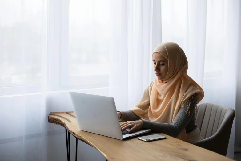 a woman sitting at a table using a laptop computer, inspired by Maryam Hashemi, trending on pexels, hurufiyya, half-body shot, islamic, slightly minimal, student