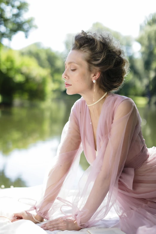 a woman in a pink dress sitting on a bed, sitting at a pond, van cleef & arpels style, elizabeth olsen, at the waterside